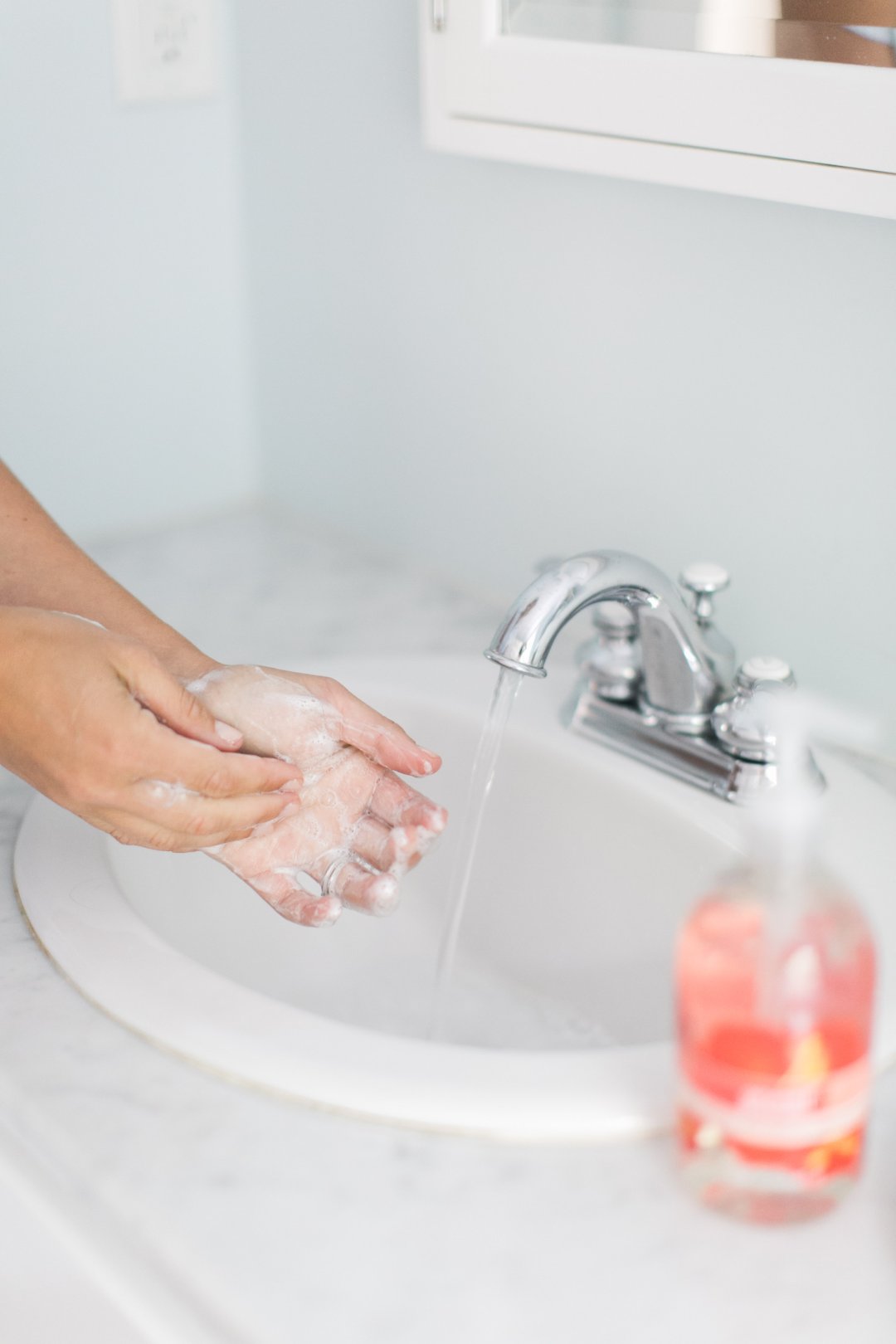 handwashing in bathroom, hand soap bottle in foreground out of focus