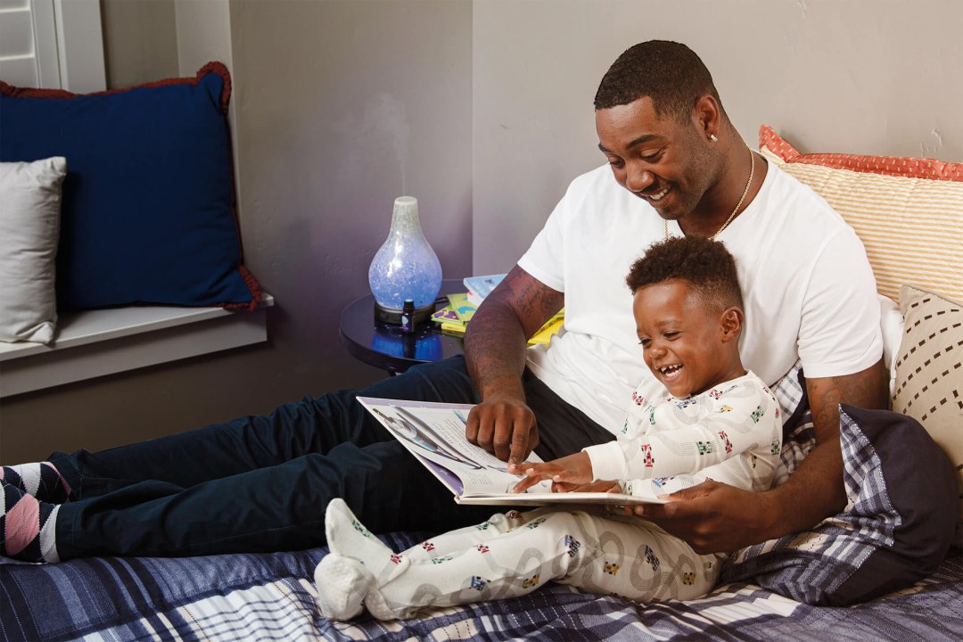 A father and his son reading bedtime stories with a Scentsy essential diffuser on the bedside table expelling the best scented essential oils from Scentsy