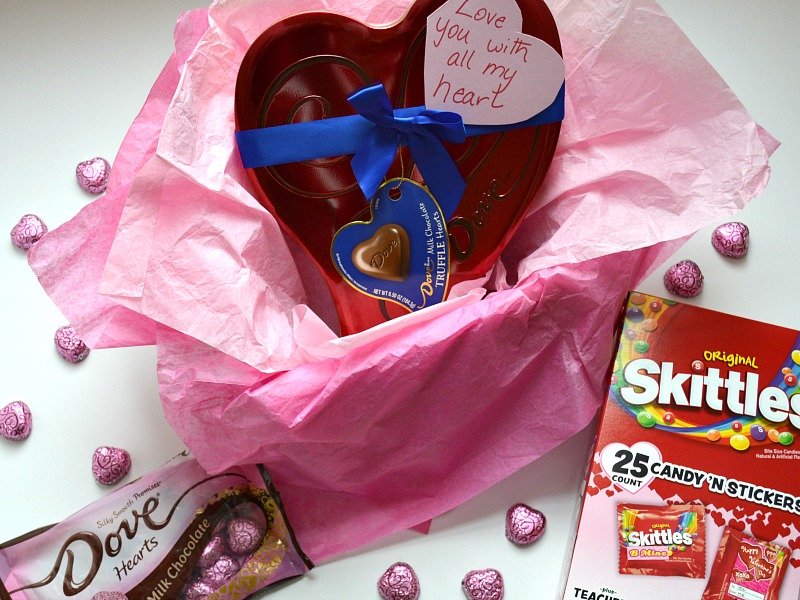 heart-shaped box of chocolate nestled in pink tissue paper with handwritten note and other candy.