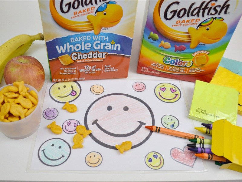 overhead view of smiley face coloring mat with crayons and snack fish crackers